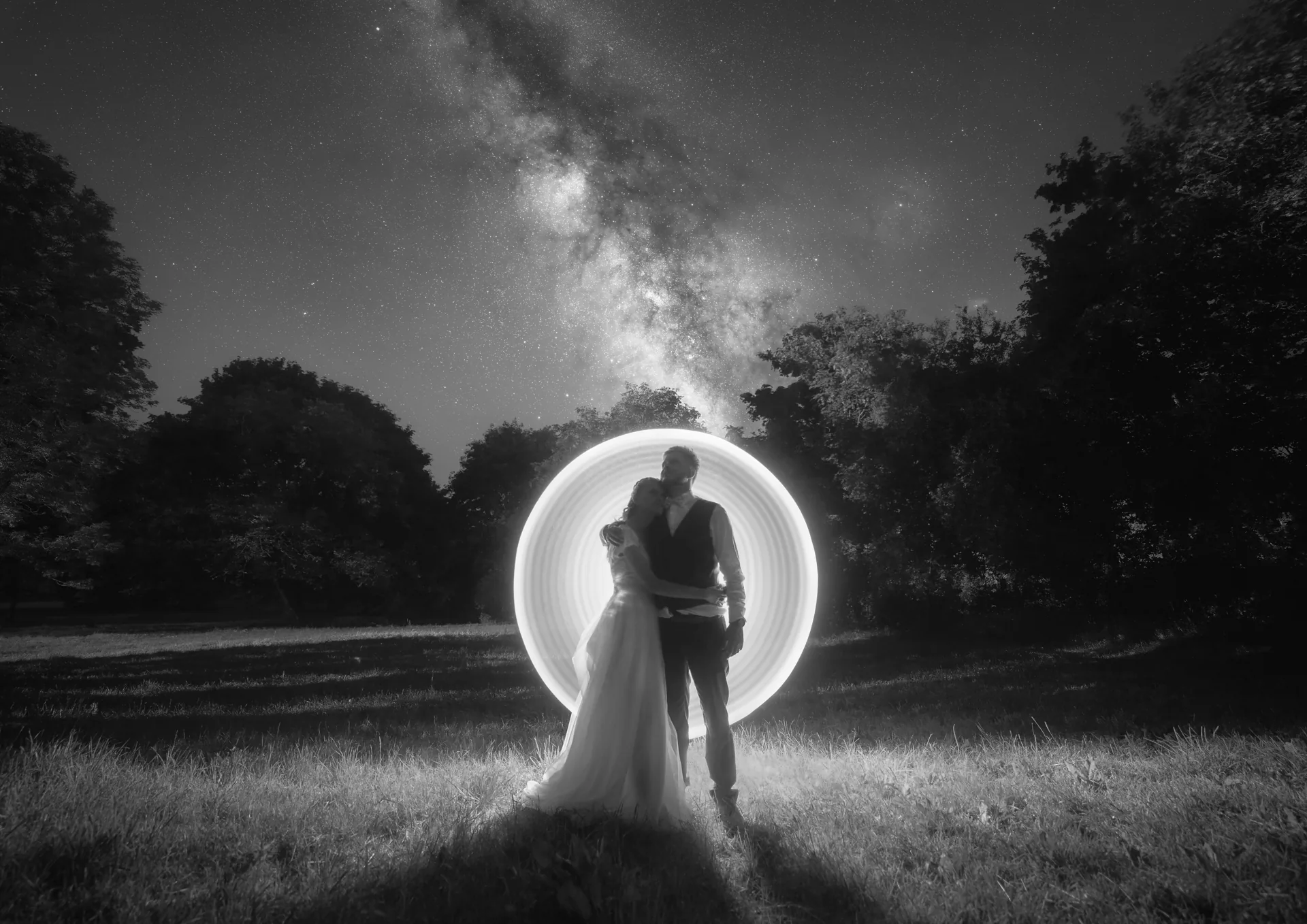 Un couple de mariés enlacé dans un cercle de lightpainting, sous la Voie lactée et un ciel étoilé.
