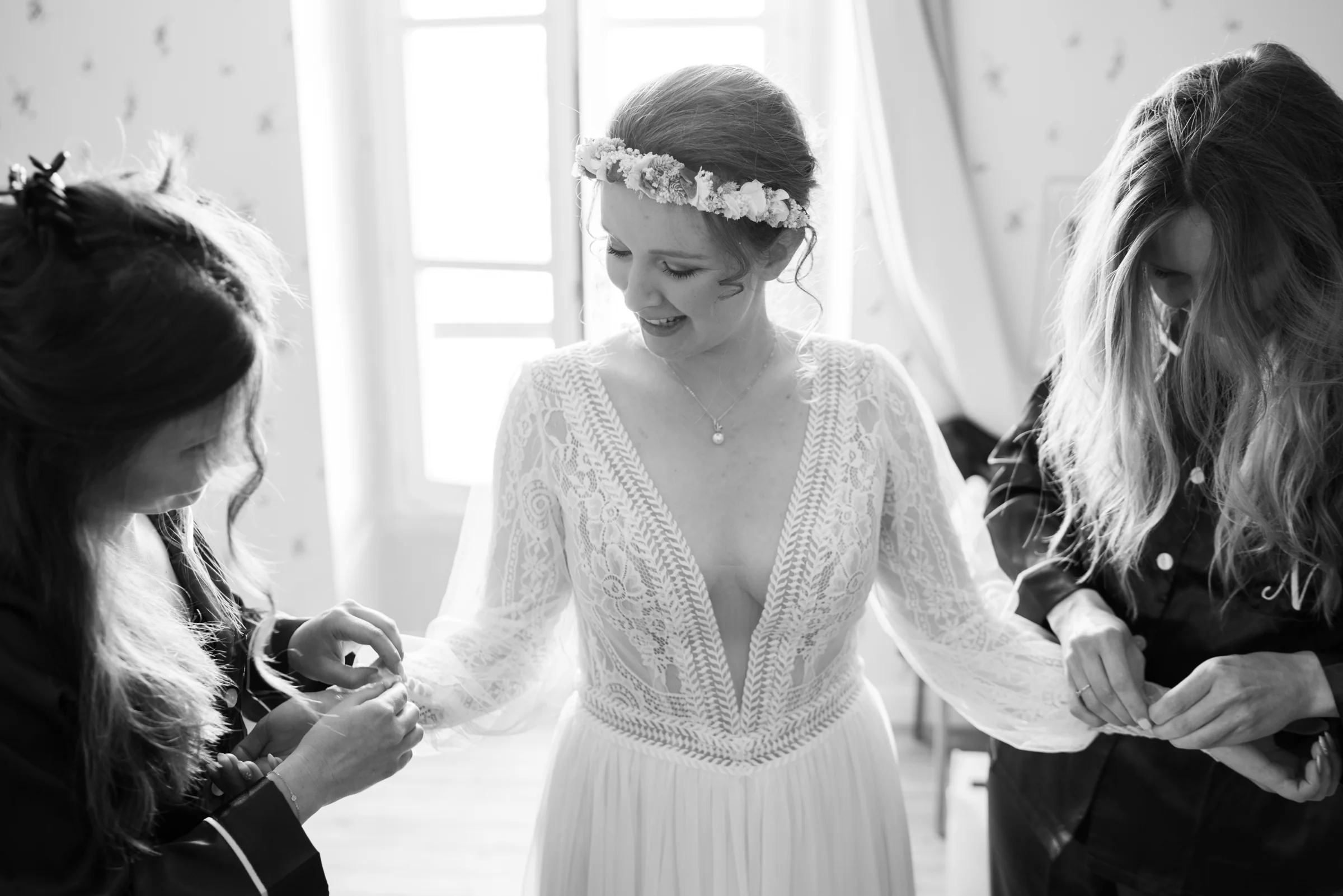 Deux proches ajustent les manches de la robe en dentelle de la mariée pendant ses préparatifs.